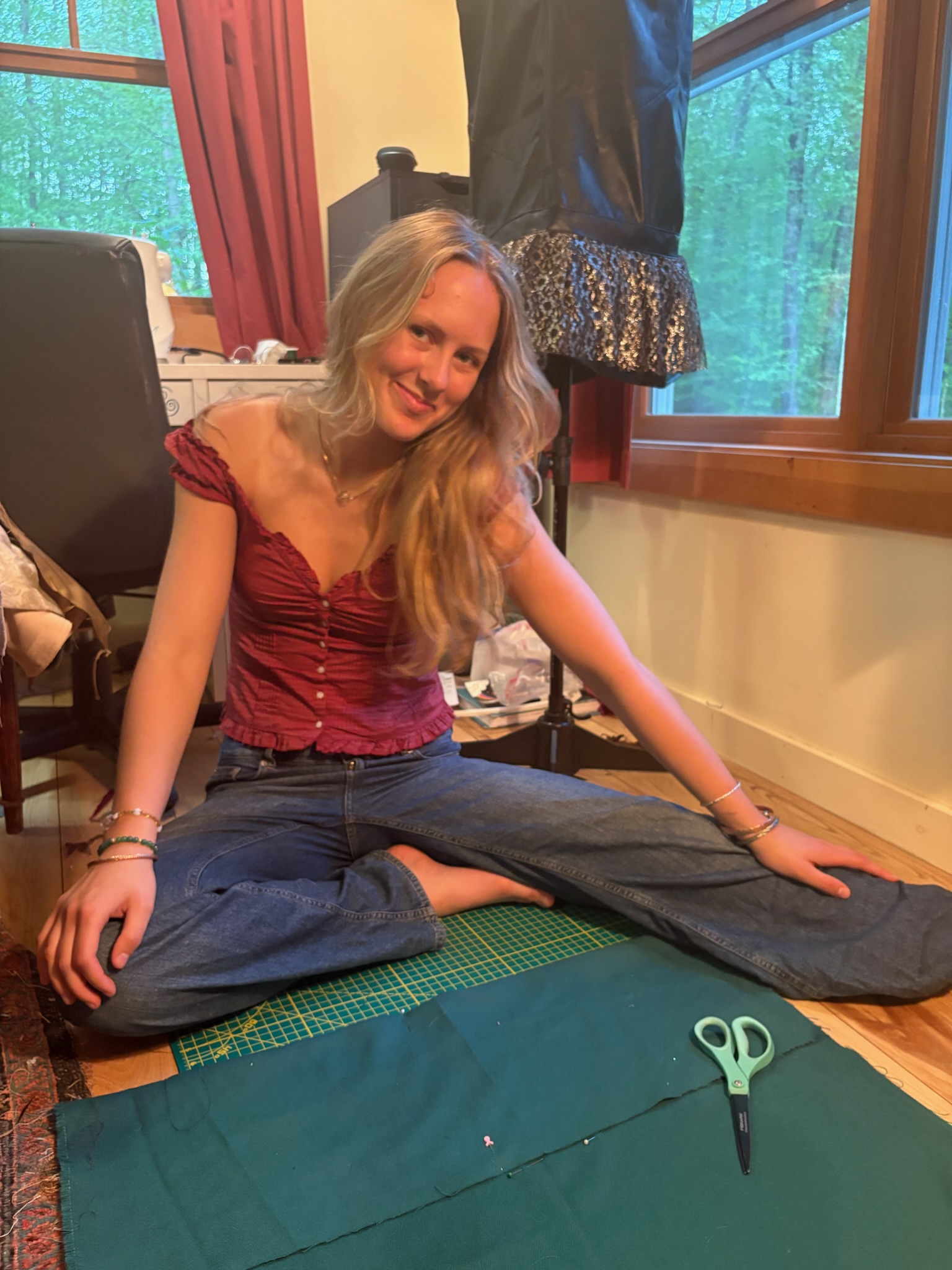 Seriena sitting on the studio floor cutting green fabric, surrounded by sewing supplies