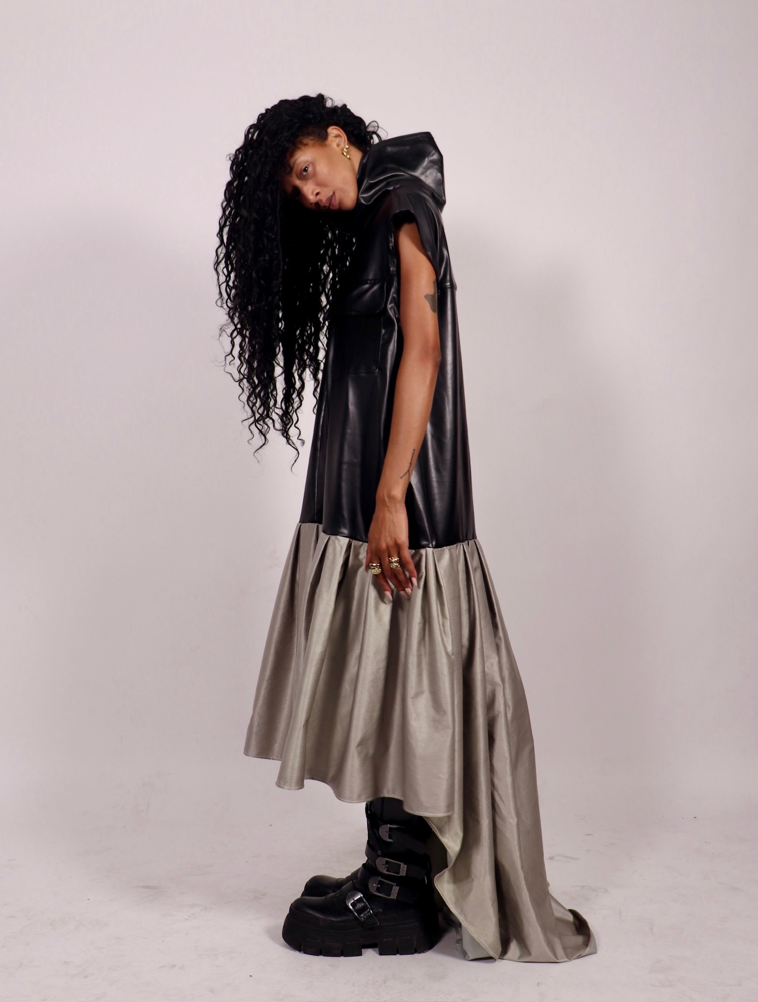 Model in a black leather-look hooded cape dress with a gray pleated train, studio shot