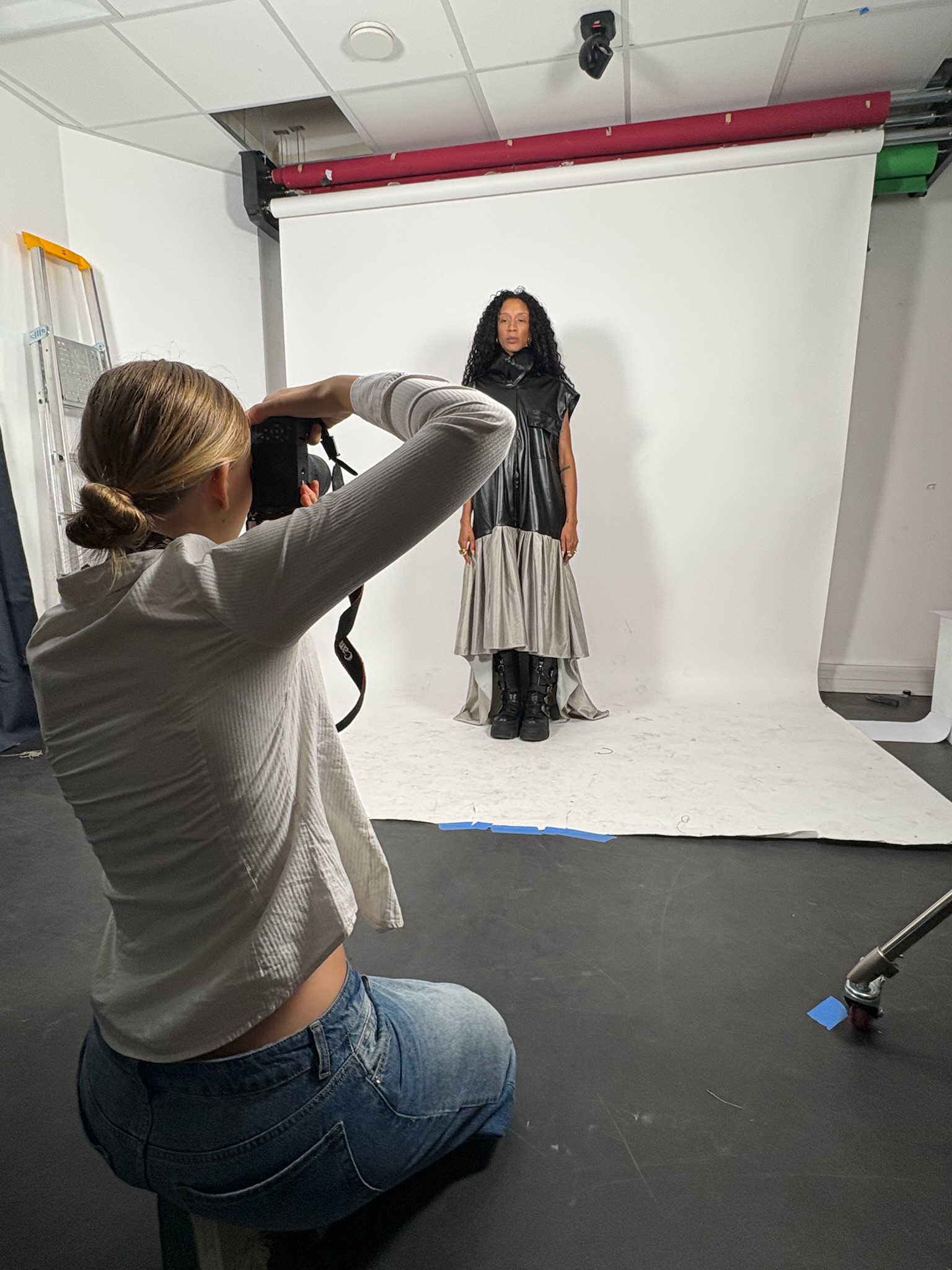 Seriena photographing a model in a black leather-look dress with a draped gray skirt in the studio