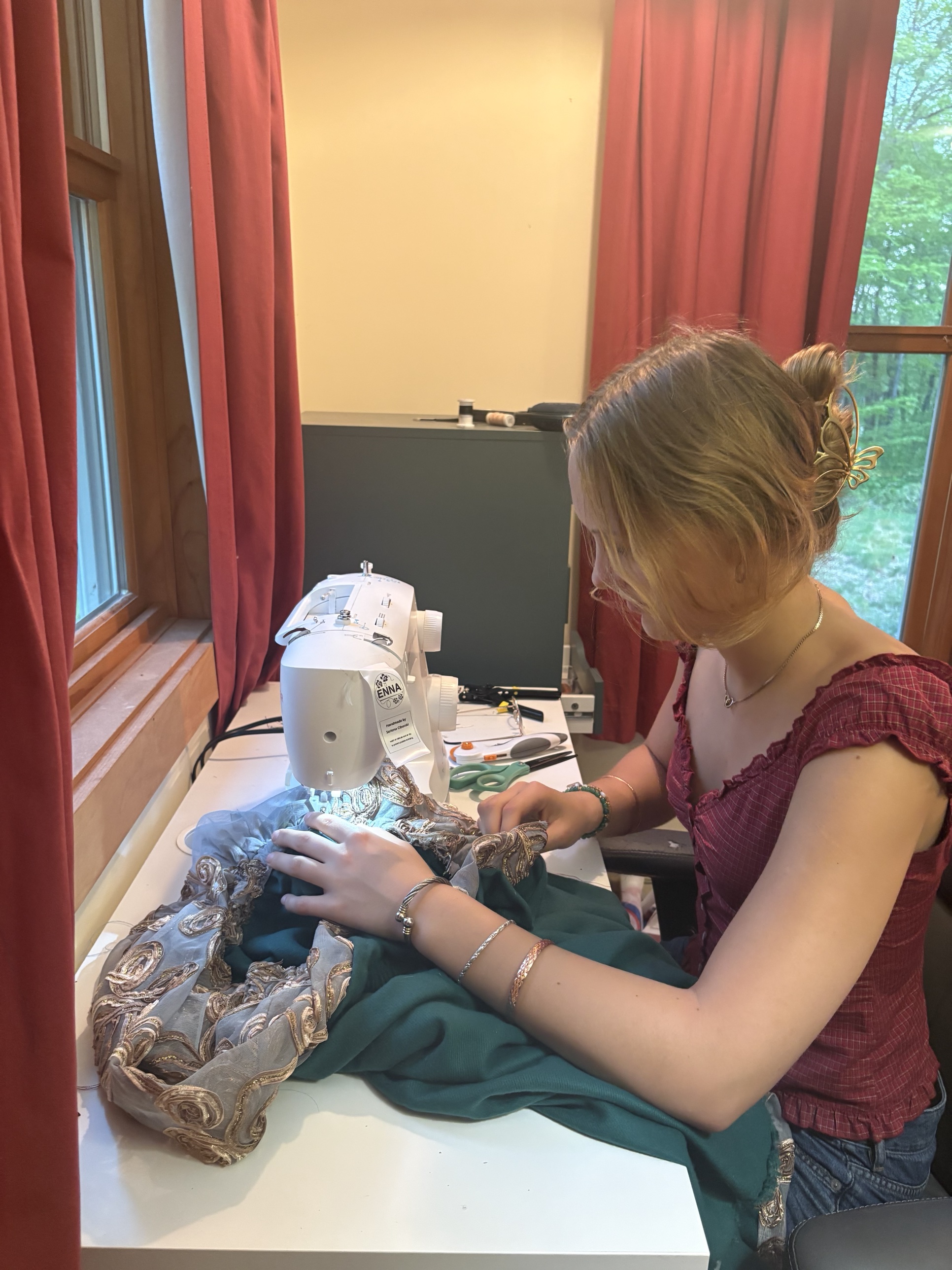 Seriena sewing a beaded gray and green garment at her machine, with the ENNA label visible