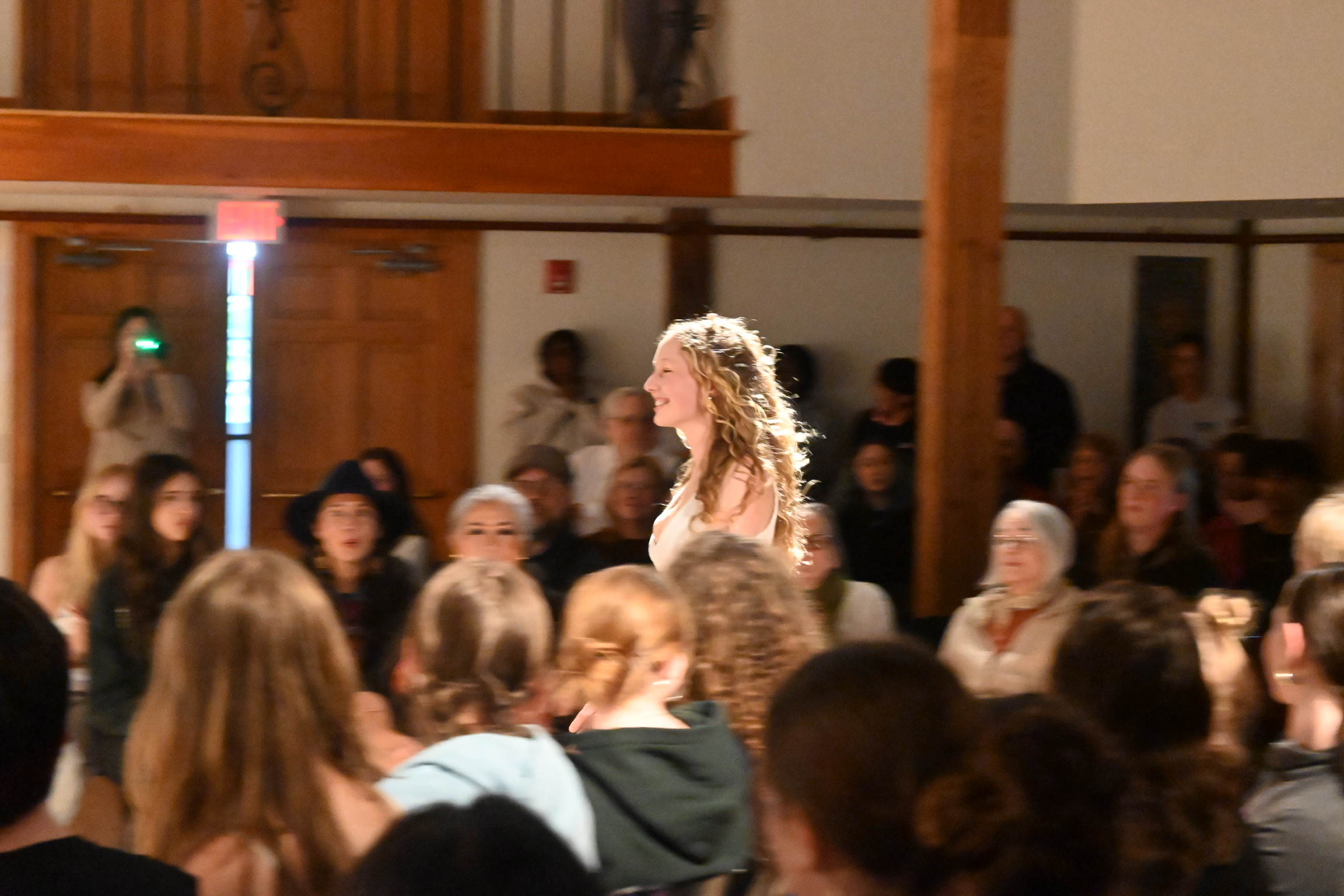 Model smiling and walking the runway through a seated audience at the ENNA senior runway show