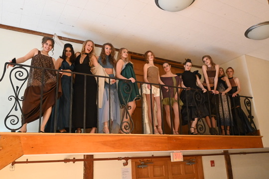 Ten models in eveningwear lined up along a balcony railing before the runway show