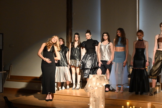 Seriena posing on stage with a line of models wearing her designs after the runway show