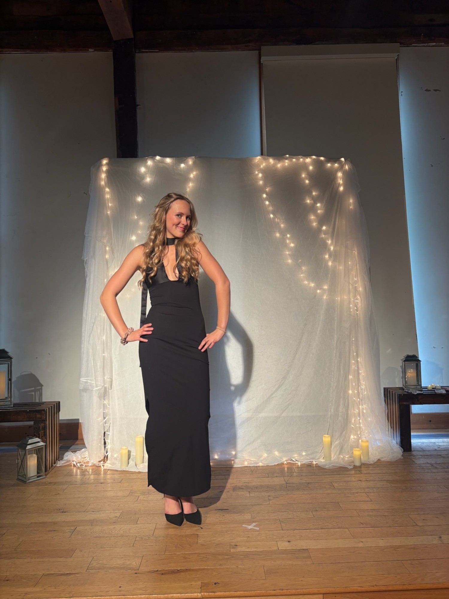Model standing in front of a fairy-lit backdrop wearing a black halter gown with a keyhole neckline