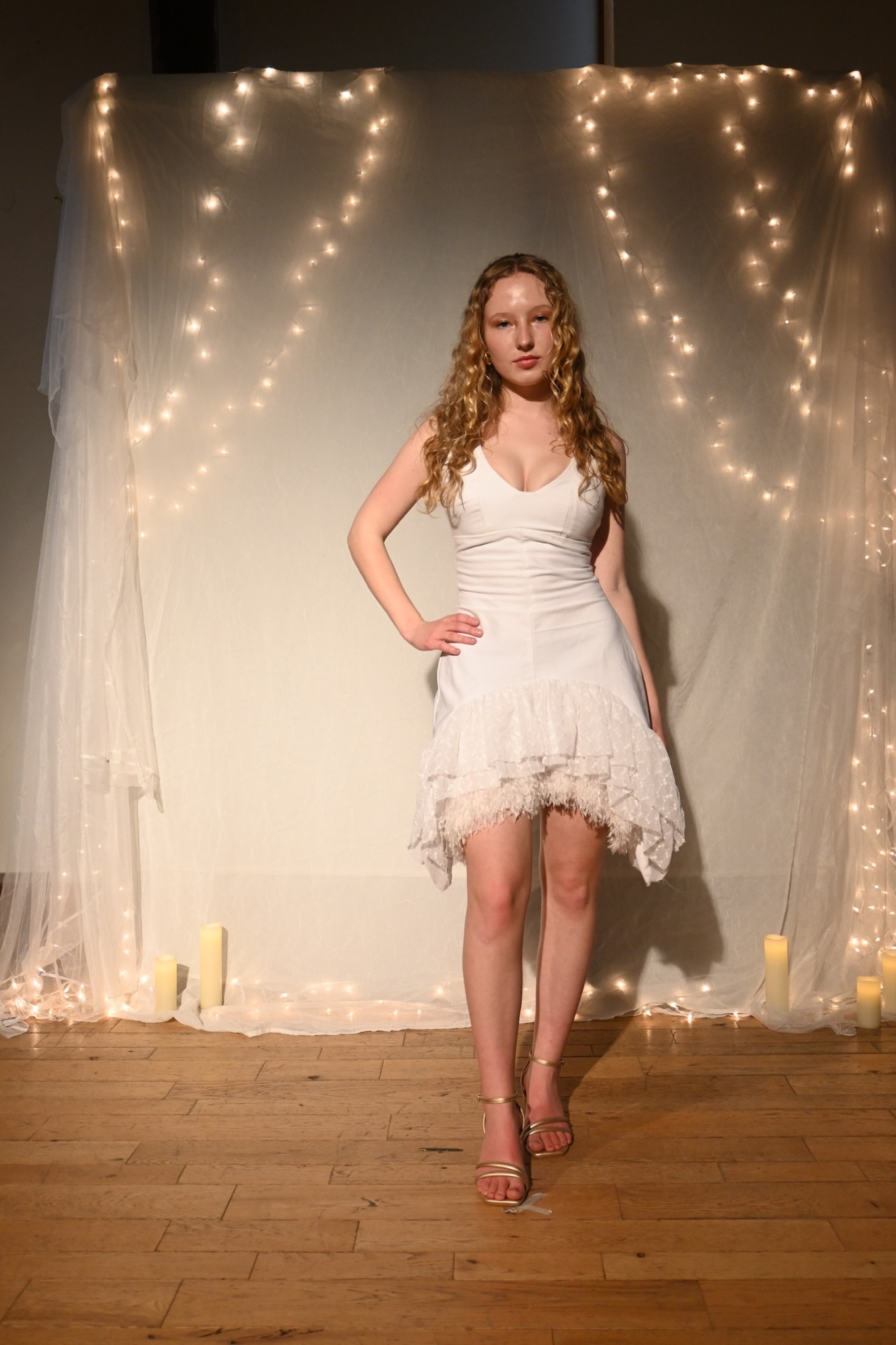 Model in a white mini dress with a lace and feather ruffle hem and gold heels, ENNA runway show