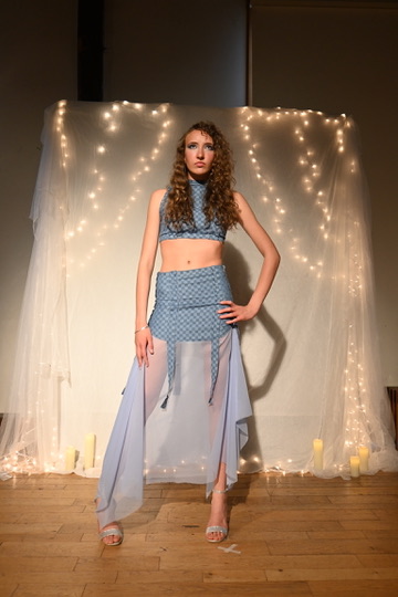 Model in a light blue textured crop top and skirt set with sheer draped side panels, ENNA runway show