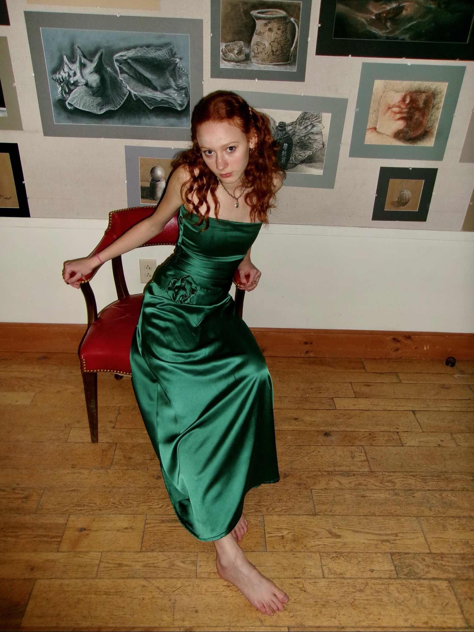 Model in an emerald green satin gown, dynamic pose against a gallery wall of sketches