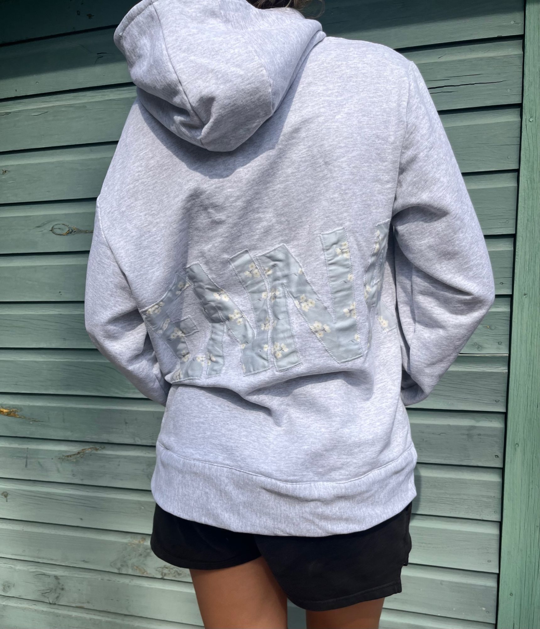 Back view of a gray hoodie with an ENNA logo appliqued in floral fabric