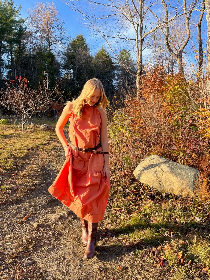 Model walking outdoors in a rust-colored belted midi dress among fall foliage