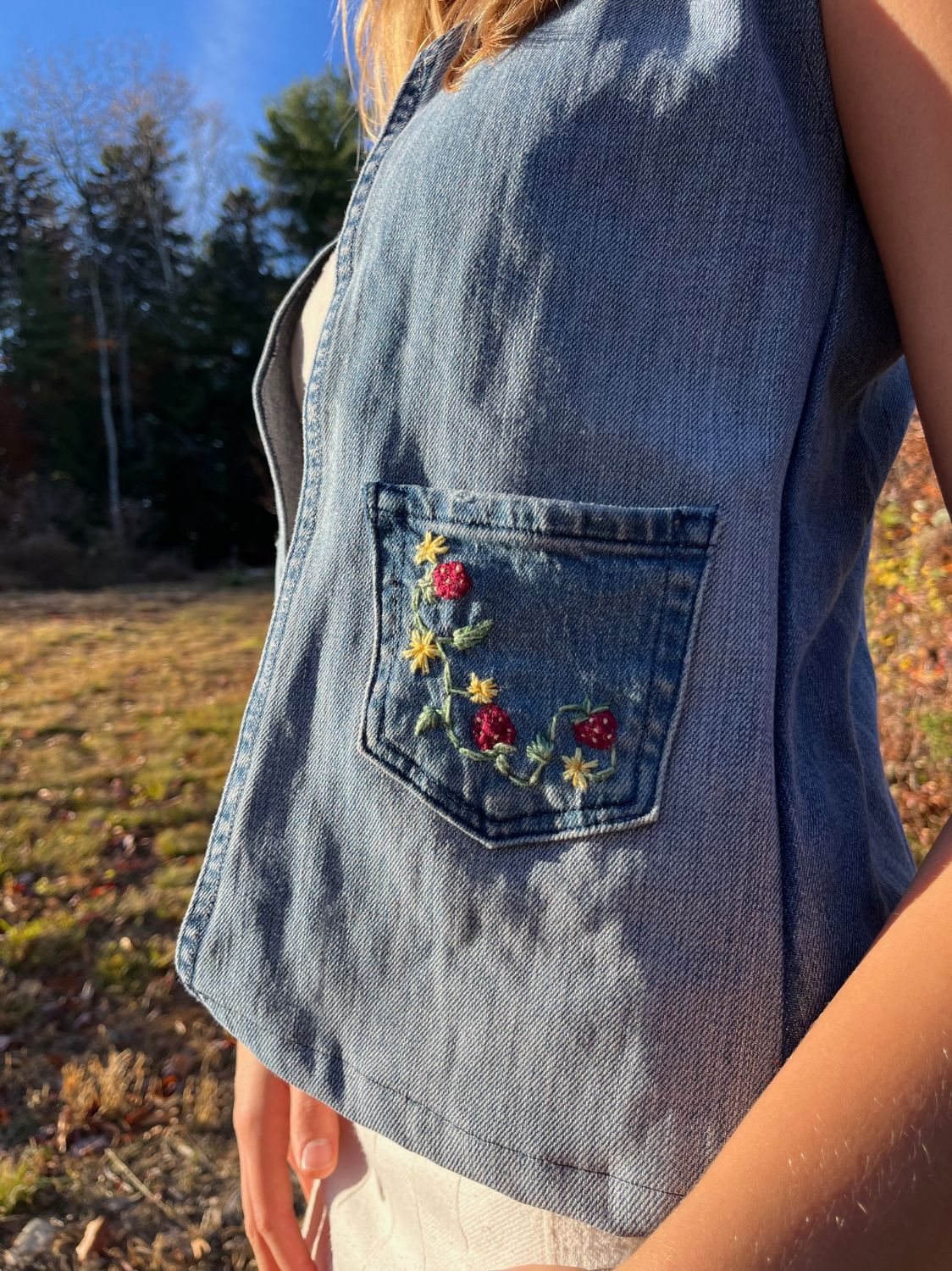 Close-up of an upcycled denim top with a hand-embroidered strawberry and flower pocket