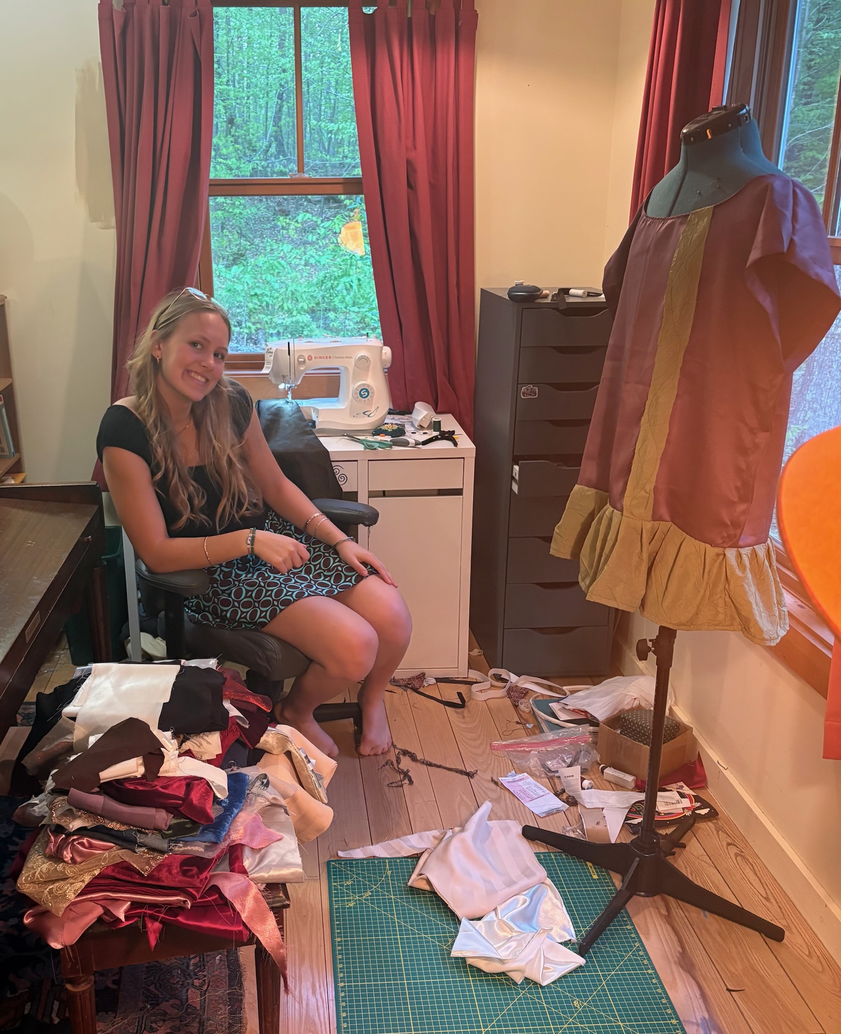 Seriena smiling in her studio, surrounded by fabric, with a garment in progress on a dress form