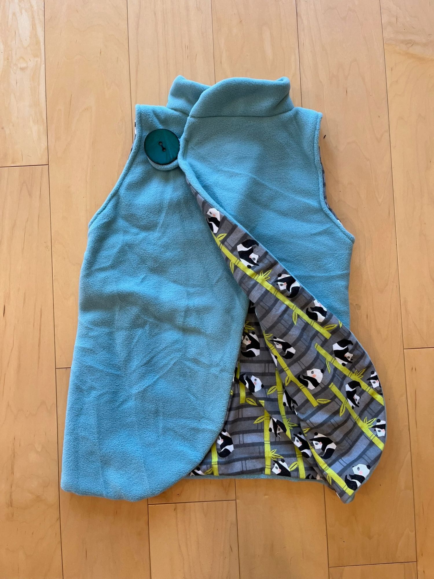 Reversible teal fleece vest with a panda and bamboo print lining, laid flat