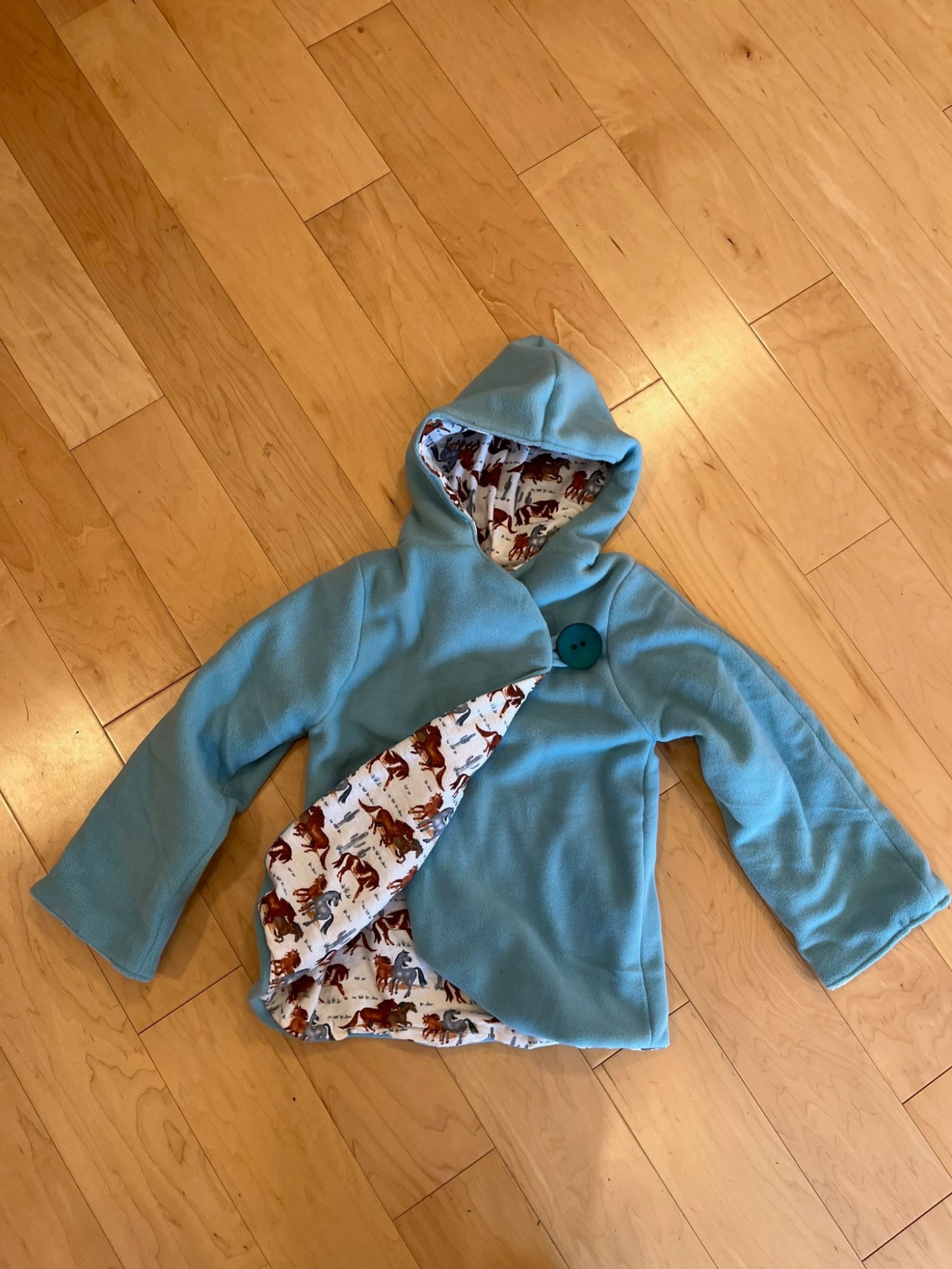 Teal hooded fleece jacket for kids with a horse print lining, laid flat